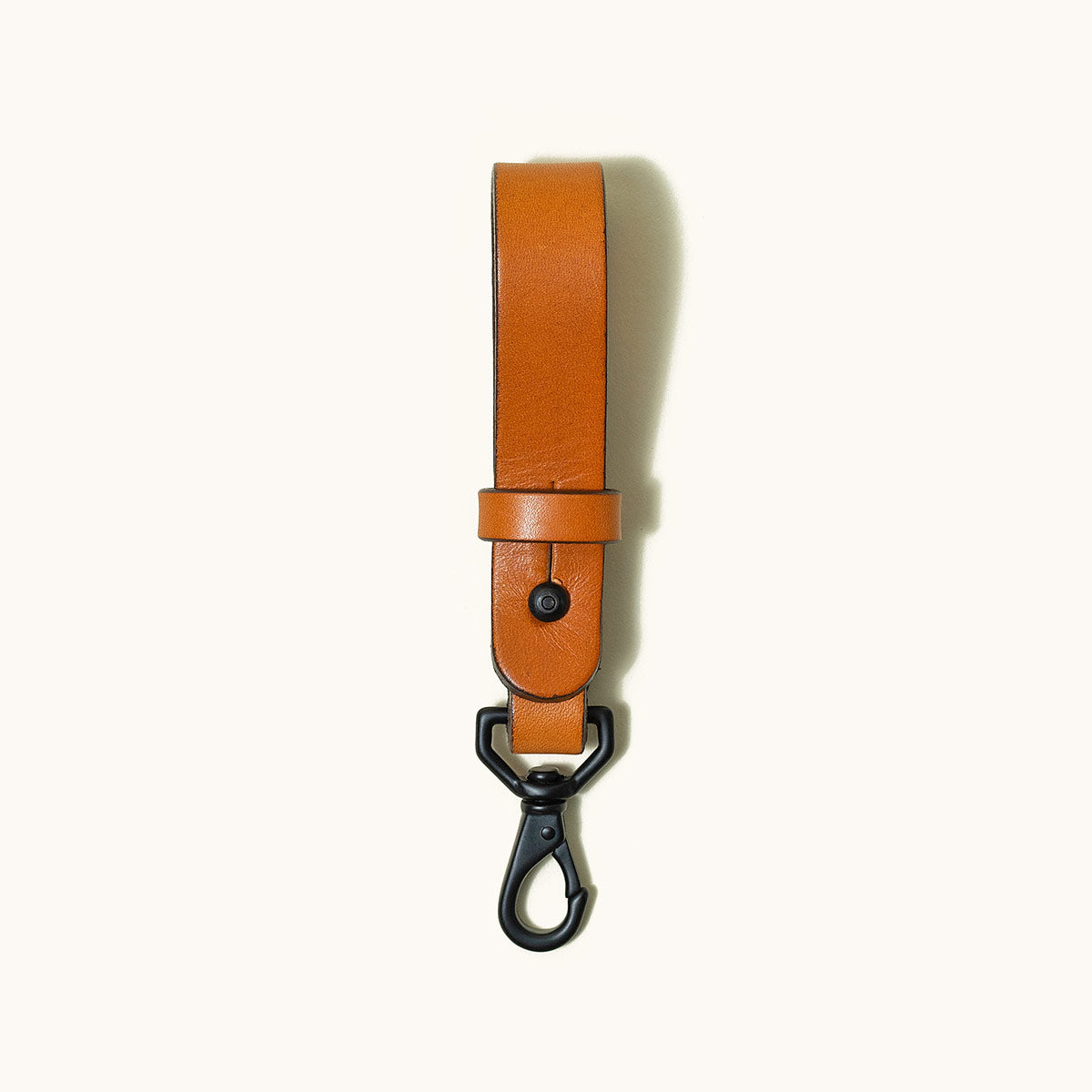 Saddle Tan leather key lanyard with a black carabiner clip and snap on a white background.