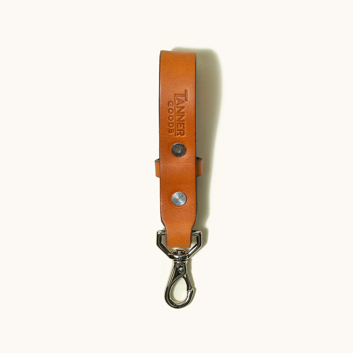 Saddle tan leather key lanyard with two silver rivets, a debossed brand logo, and a swivel snap hook.