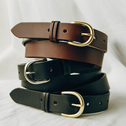 Cognac leather Meridian belt with a gold buckle, stacked above two black leather belts with silver and gold buckles.