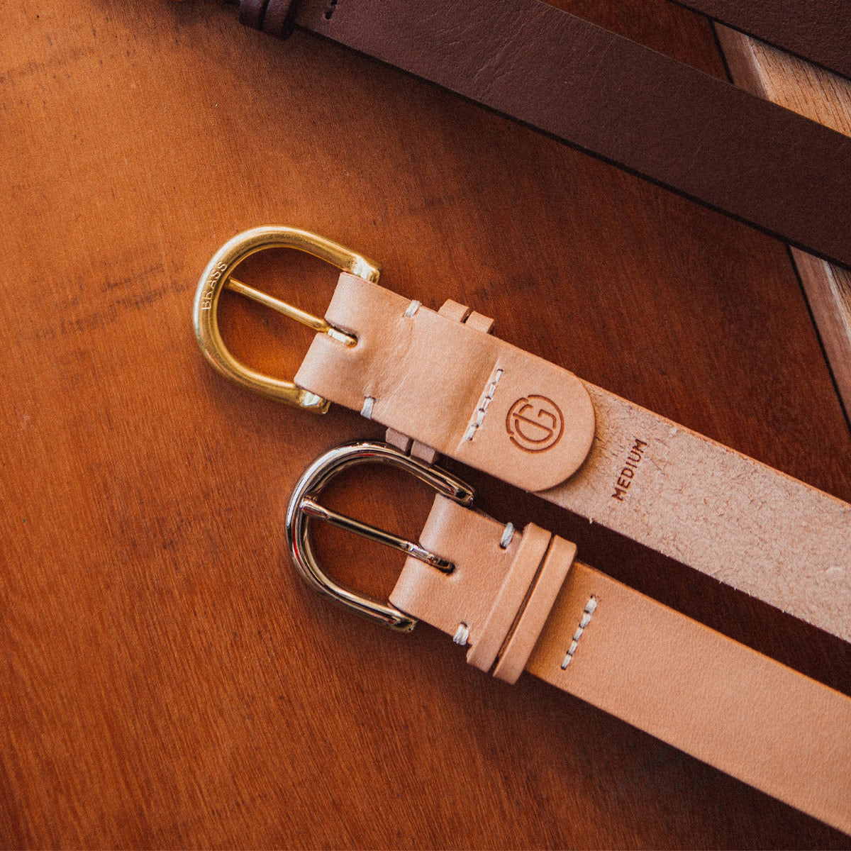 Natural Meridian leather belt with brass and silver-toned buckles, embossed 'BRASS', and initial logo.