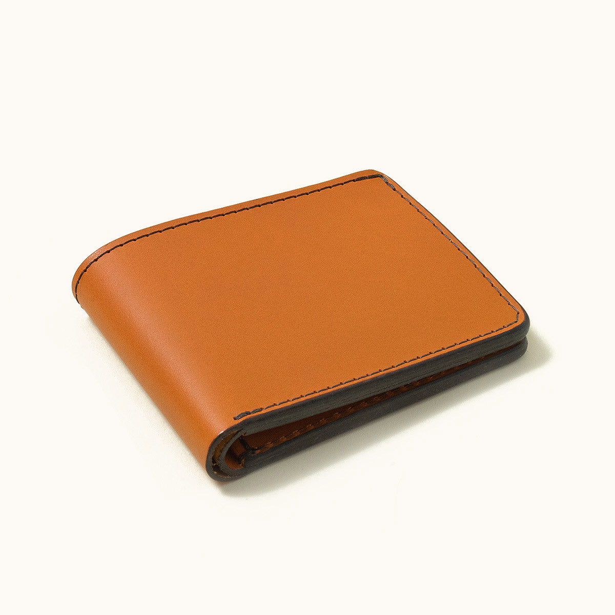 Saddle tan bifold wallet with smooth leather, dark stitching, and dark finished edges, shown closed.