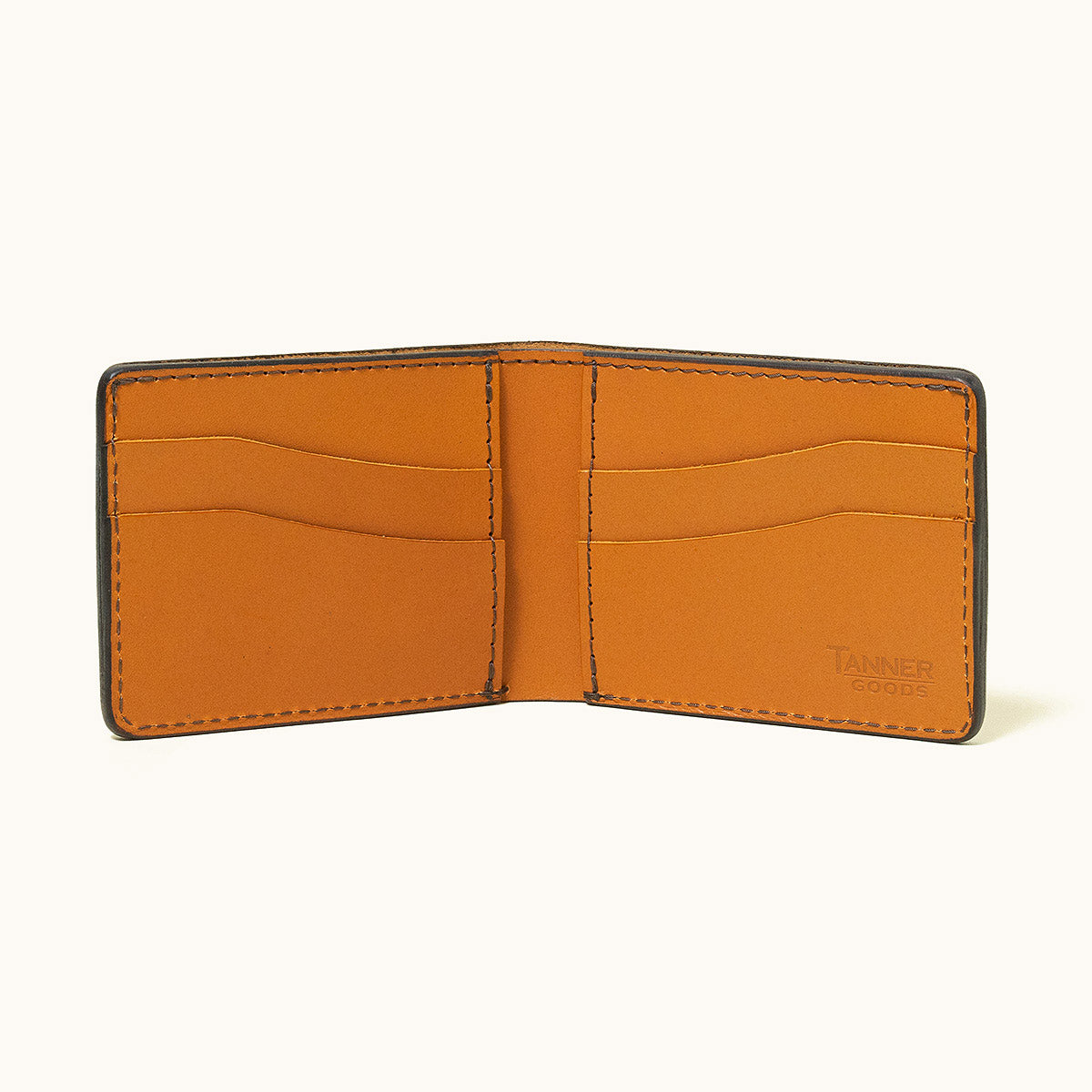 Saddle Tan Utility Bifold wallet by TANNER GOODS, open to reveal card slots and its dark exterior.