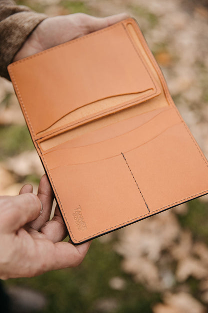Saddle tan leather Travel Wallet by Tanner Goods, open to reveal card slots and dark contrast stitching, held by hands.