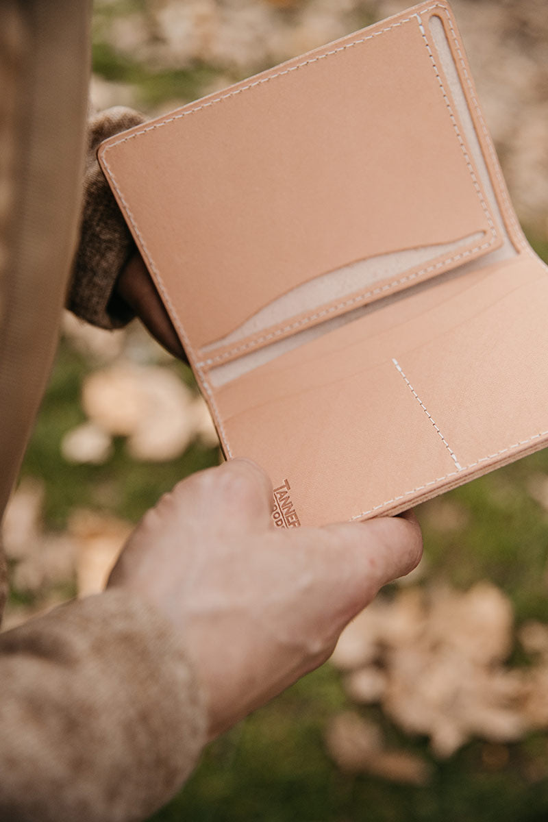 Natural leather travel wallet by Tanner Goods, held open to reveal card slots and cream stitching.