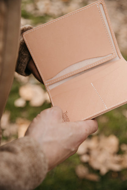 Natural leather travel wallet by Tanner Goods, held open to reveal card slots and cream stitching.