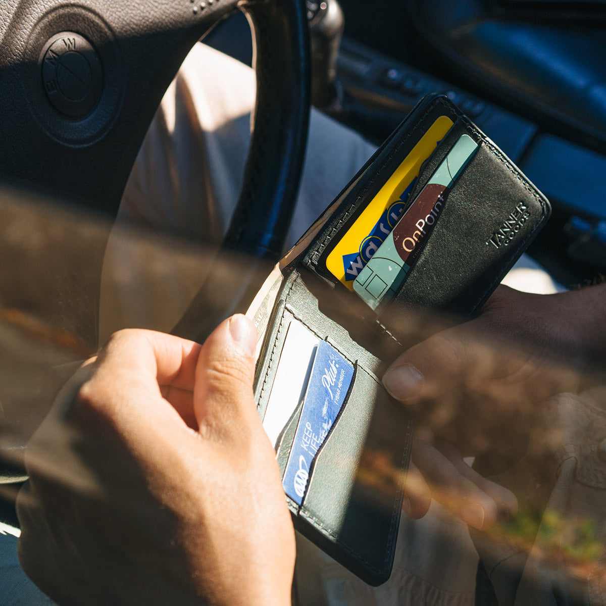 Looking through a driver's side window showing a person looking through the credit cards in their black leather Bifold wallet.