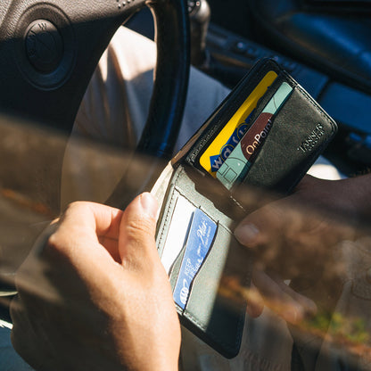 Looking through a driver's side window showing a person looking through the credit cards in their black leather Bifold wallet.
