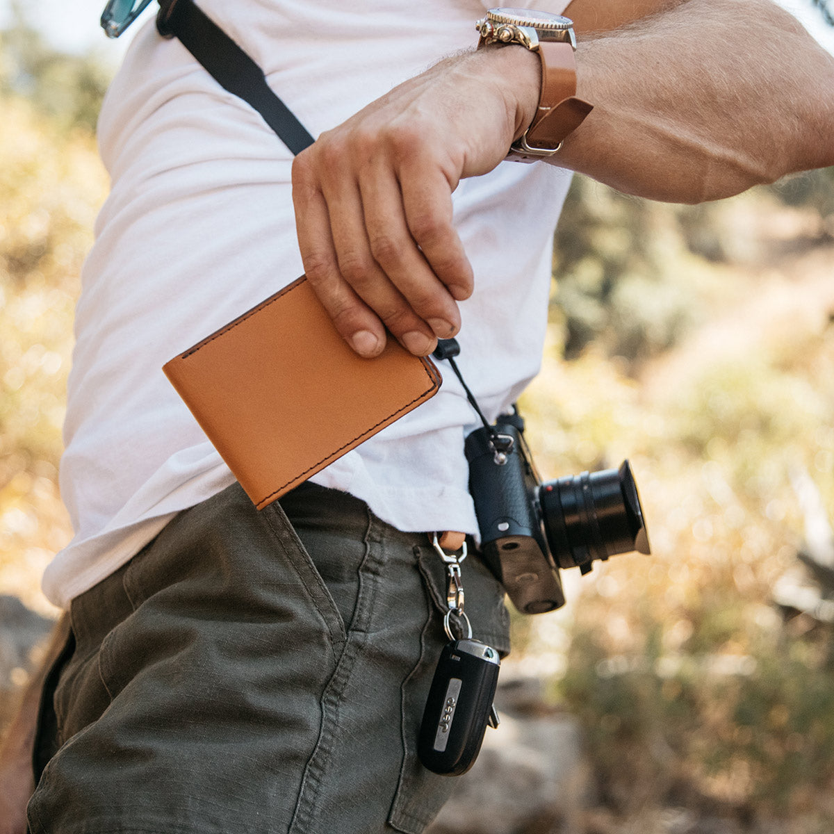 Saddle Tan Utility Bifold wallet with dark stitching and black cord, held in a man's hand.