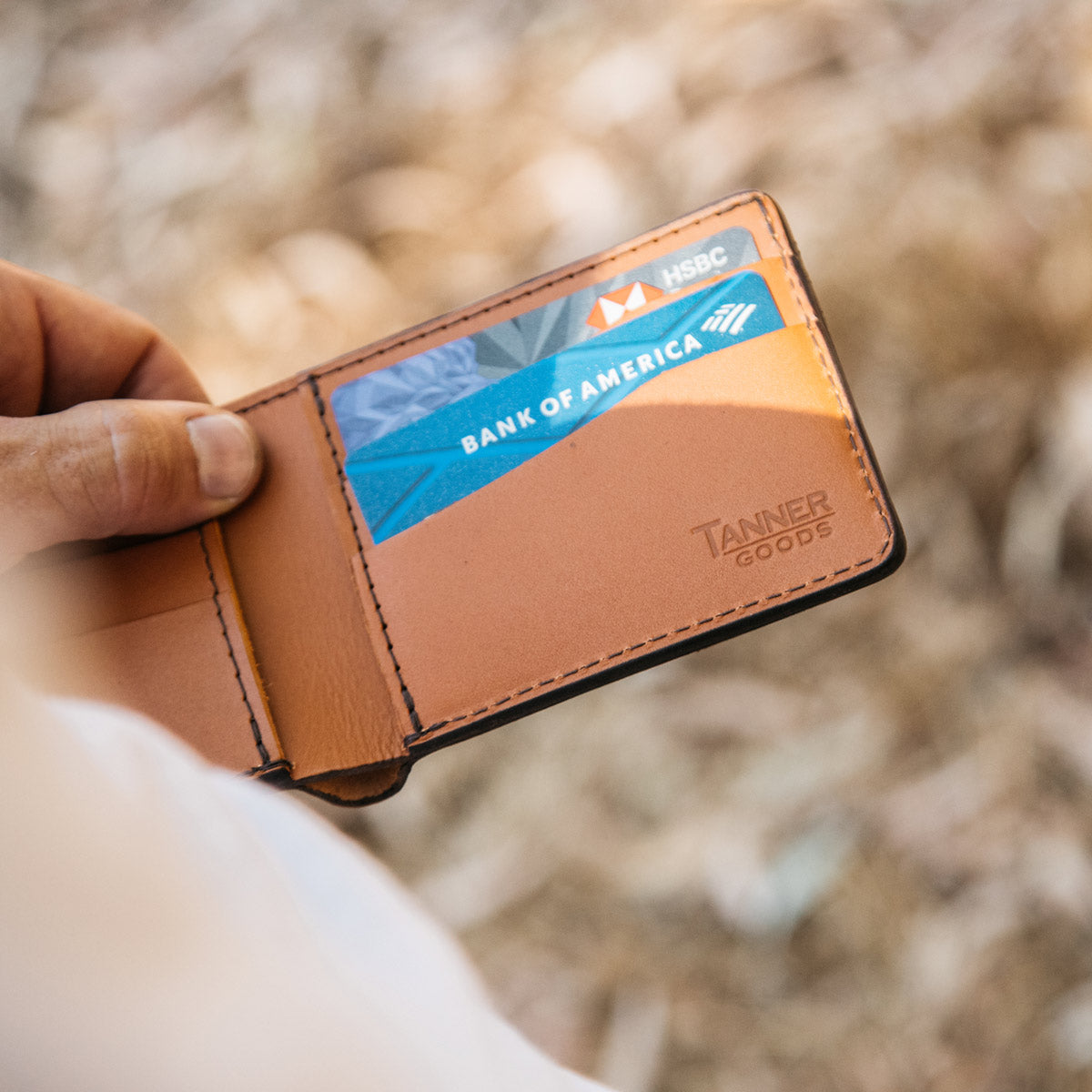 Saddle Tan leather bifold wallet from Tanner Goods, open with credit cards inside, held by a hand.