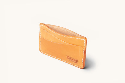 Golden leather wallet with multiple card slots and white stitching, featuring an embossed 'Tanner Goods' logo on the front.