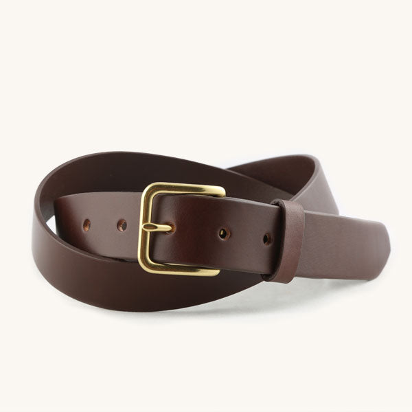 Cognac leather belt with a gold rectangular buckle, casually coiled on a white background, showing punched holes.