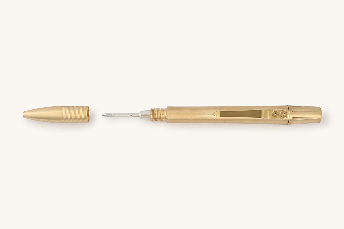 Brass mechanical pen by Memori Mechanico, lying horizontally with its cap removed, revealing the silver pen tip and pocket clip.