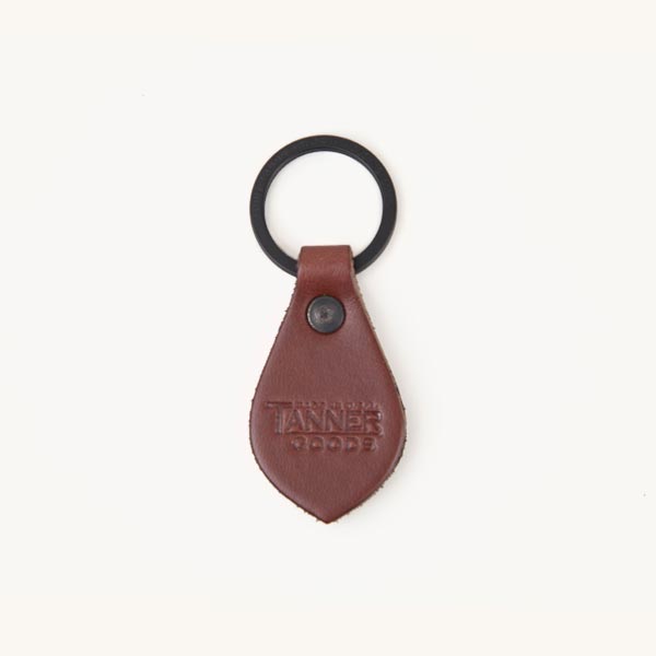 Cognac leather Key Fob with a teardrop shape, black metal ring, and embossed text "TANNER GOODS".