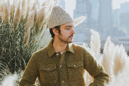 Off-white cable knit cap with a textured pattern, worn by a man.