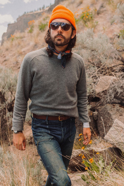 Cognac leather belt with a gold buckle, worn with dark blue jeans and a grey sweater.