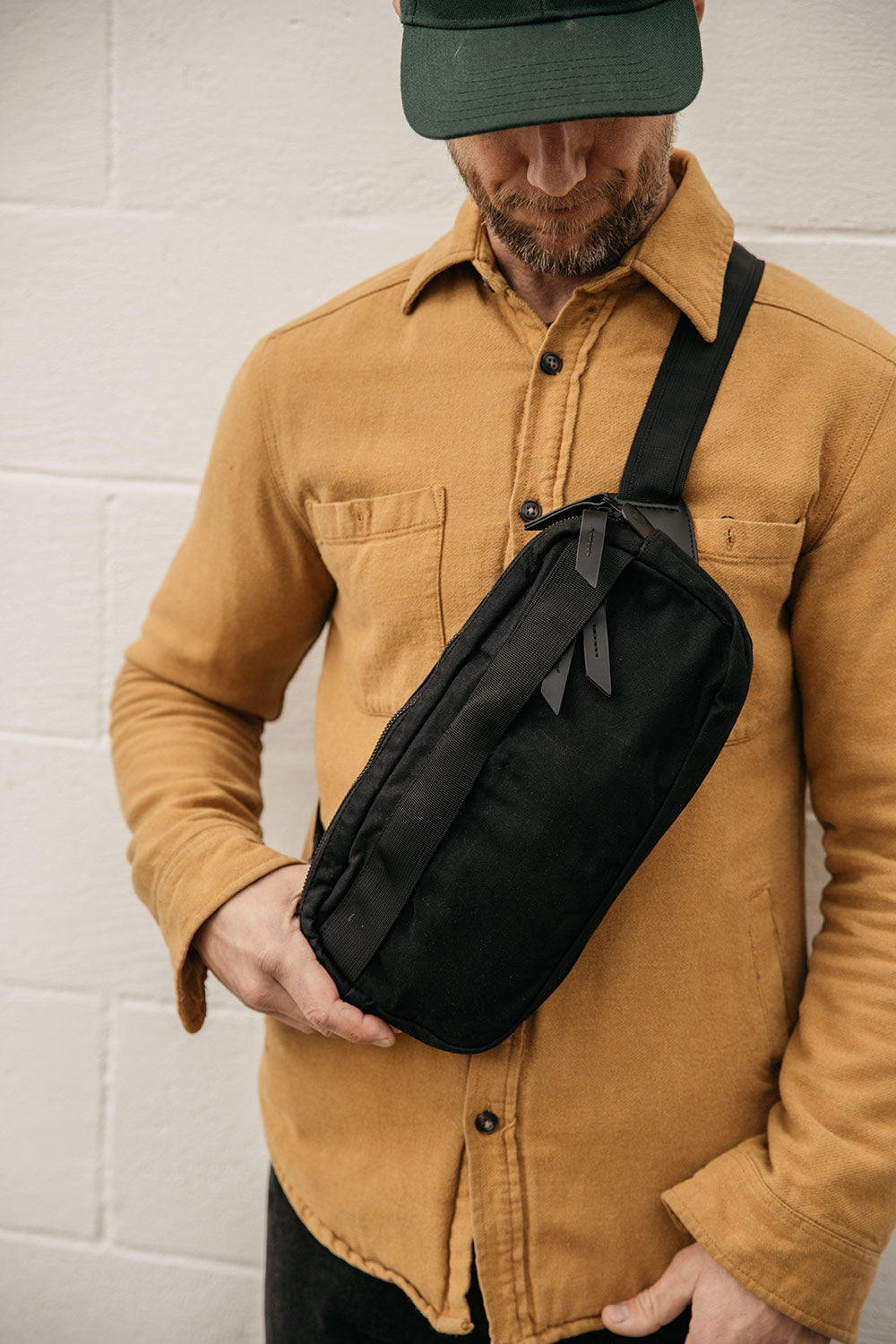 Black waxed canvas Canyon Crossbody Pack with zipper pulls, worn cross-body by a man in a mustard yellow shirt.