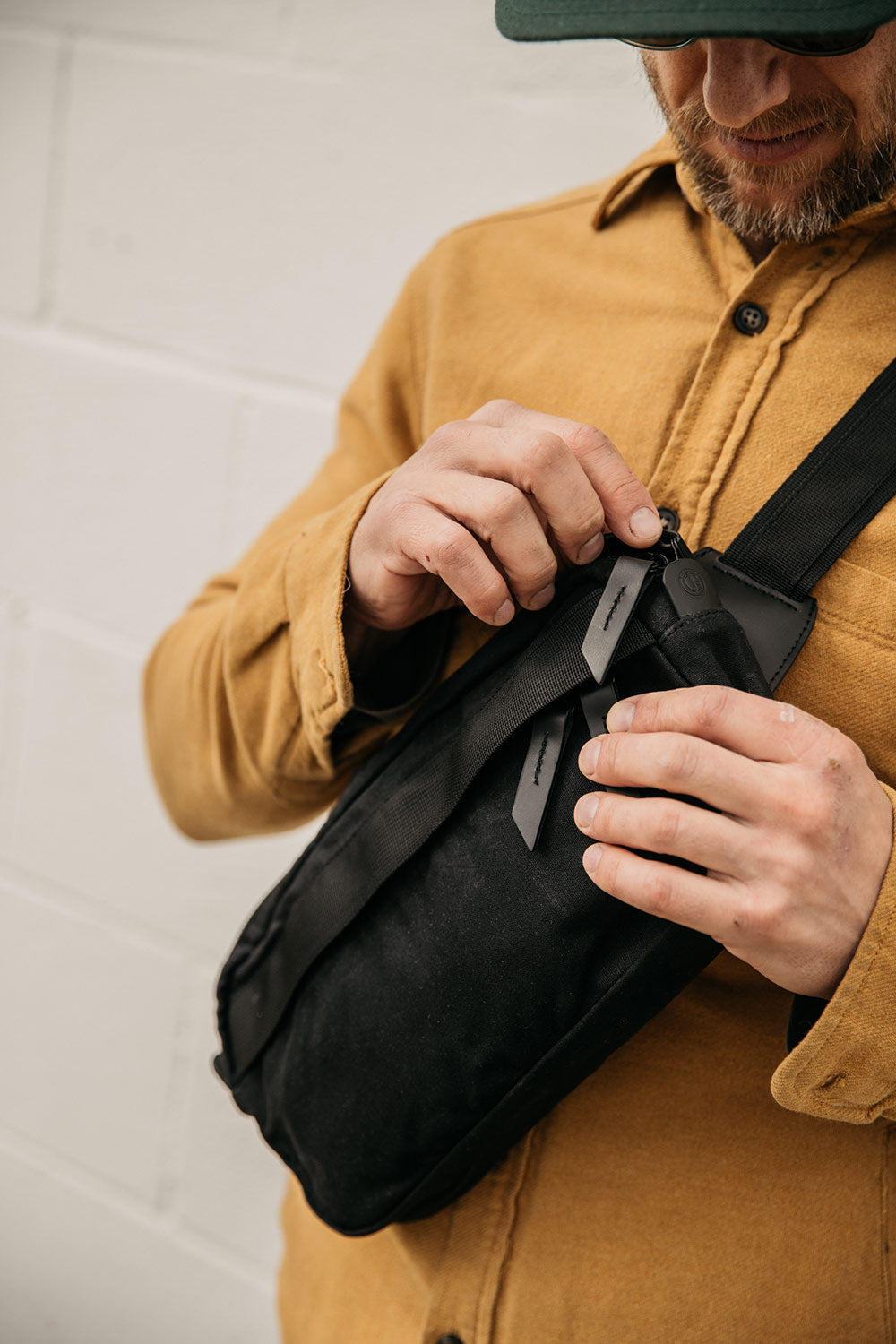 Black waxed canvas Canyon Crossbody Pack, worn by a man in a yellow shirt, being opened at the zipper.