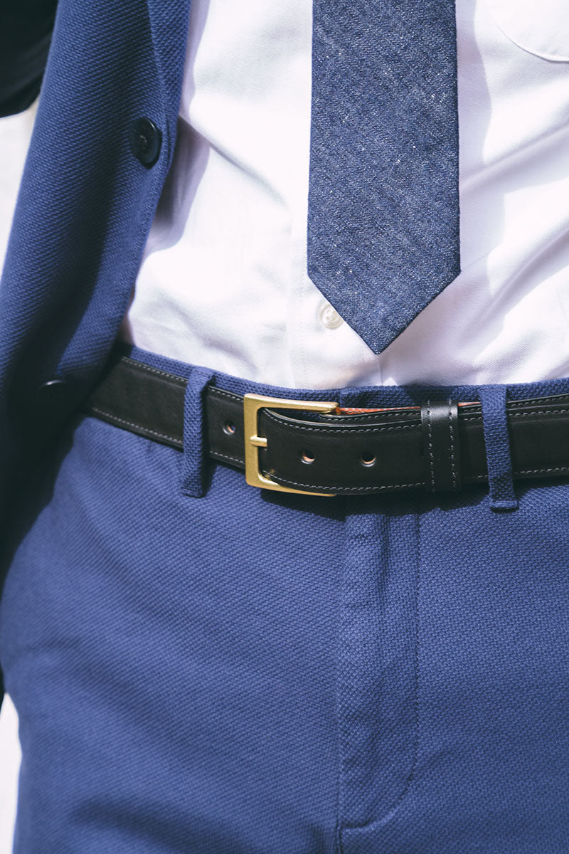 Black dress belt with a gold buckle, styled with a blue suit, white shirt, and blue tie.
