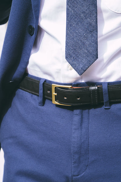 Black leather dress belt with a gold buckle, worn with blue textured trousers, a white shirt, and a blue blazer.