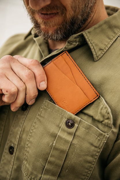 Saddle tan leather wallet by Tanner Goods being placed into a man's olive green shirt pocket.