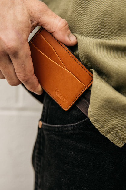 Saddle Tan leather wallet by Tanner Goods being placed into a black jeans pocket, worn with a green shirt.