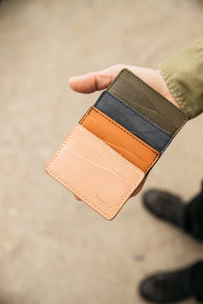 Saddle Tan leather Journeyman wallet by Tanner Goods, stacked with natural, grey, and olive wallets in a hand.
