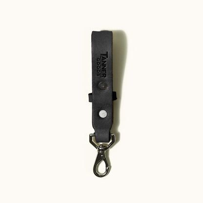 Black leather Key Lanyard by Tanner Goods, embossed with logo, featuring two silver rivets and a metal carabiner clip.