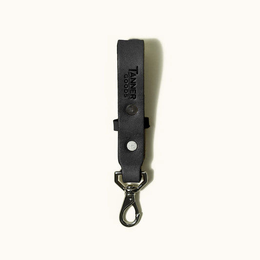 Black leather Key Lanyard by Tanner Goods, embossed with logo, featuring two silver rivets and a metal carabiner clip.