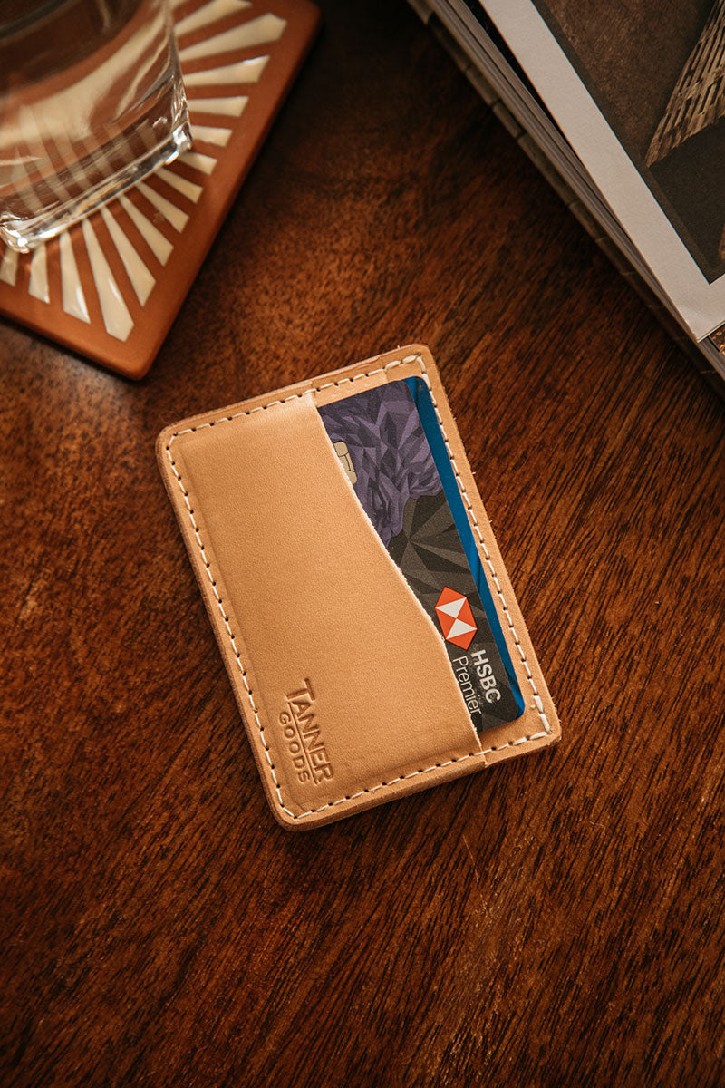Natural leather minimalist wallet by Tanner Goods, with an HSBC Premier card visible, on a wooden table.