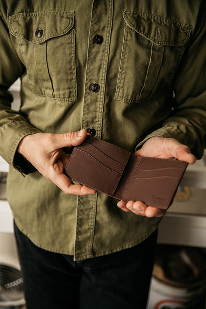 Cognac recycled leather utility bifold wallet held open to show multiple card slots, in the hands of a person wearing an olive utility shirt.
