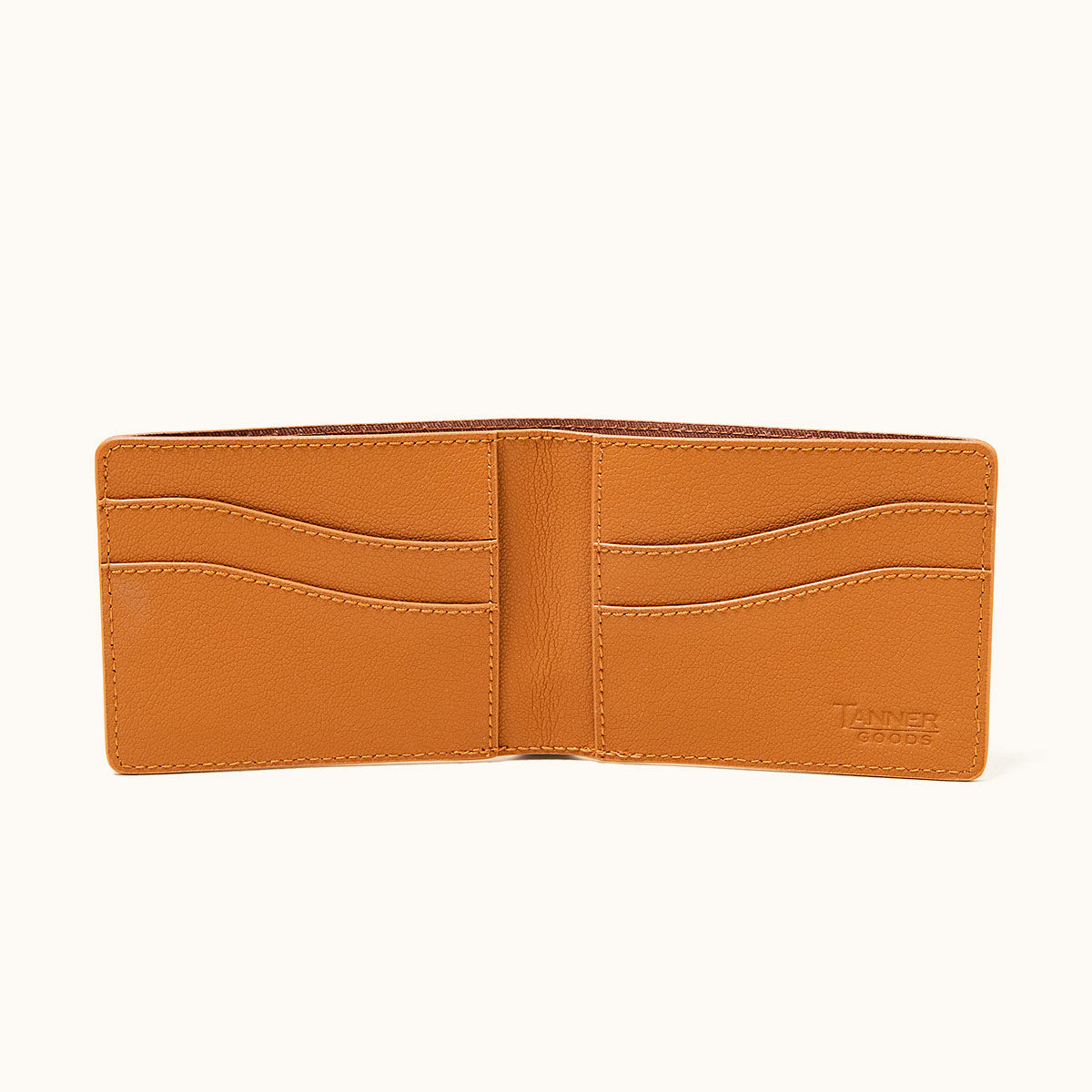 Saddle tan recycled leather bifold wallet by TANNER GOODS, open to show multiple card slots and bill compartment.