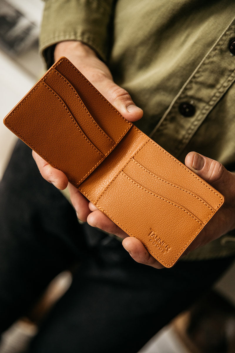 Saddle tan recycled leather bifold wallet by TANNER GOODS, showing multiple card slots, held open in hands.