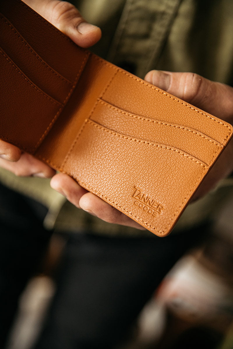 Saddle tan recycled leather bifold wallet by Tanner Goods, held open, revealing textured leather and multiple card slots.