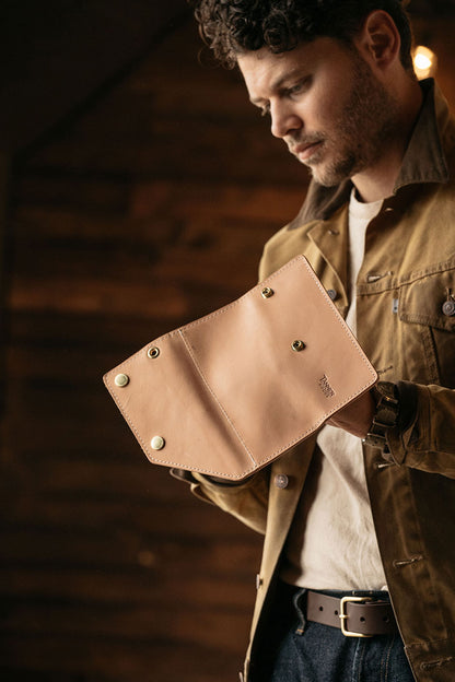 Natural leather workman's wallet by Tanner Goods, held open by a man in a brown jacket.