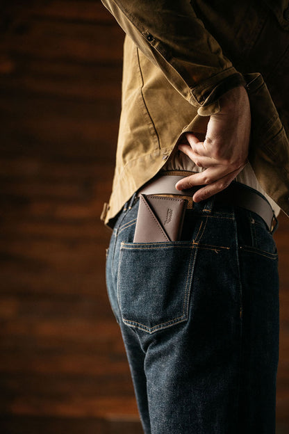 Cognac Workman Wallet with a diagonal flap, tucked into the back pocket of dark jeans, next to a hand and a brown jacket.