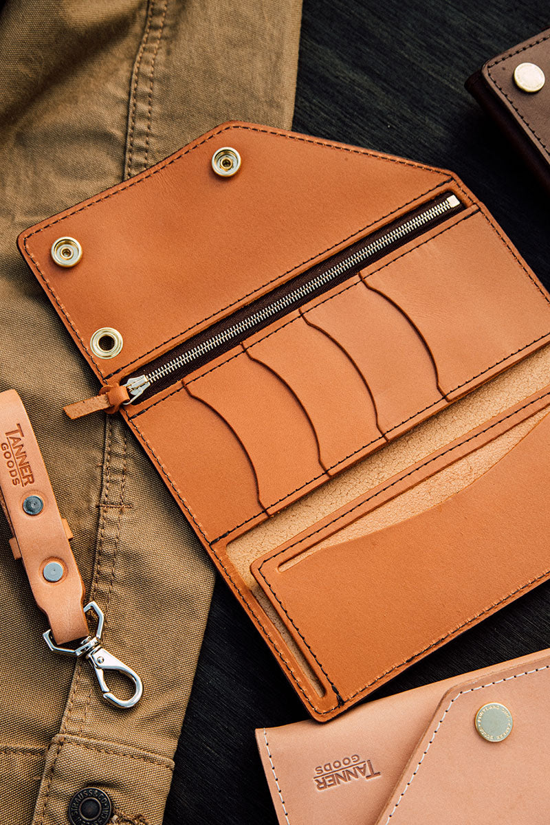 Saddle tan leather Workman Wallet, open to reveal multiple card slots, a zippered compartment, and brass snap closures.