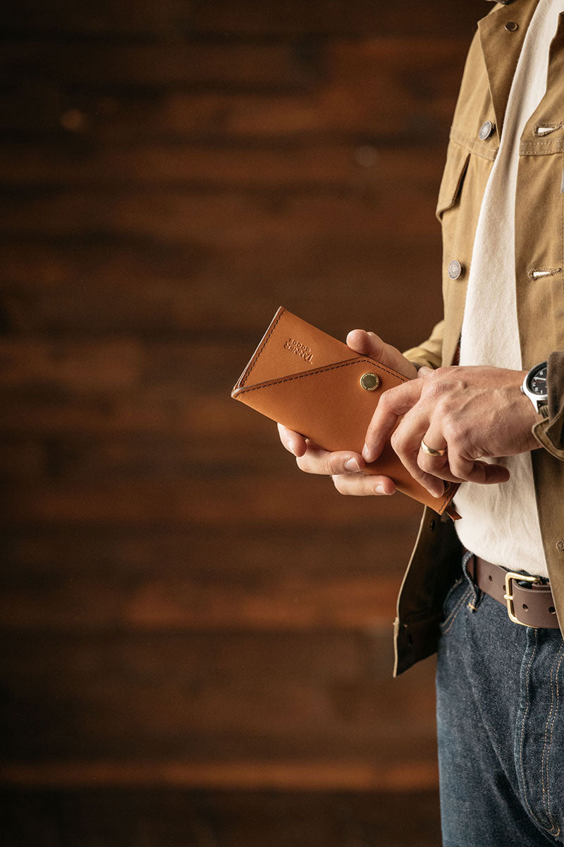 Saddle tan leather Workman Wallet by Tanner Goods, with a visible stamped logo and metal snap, held in hands.