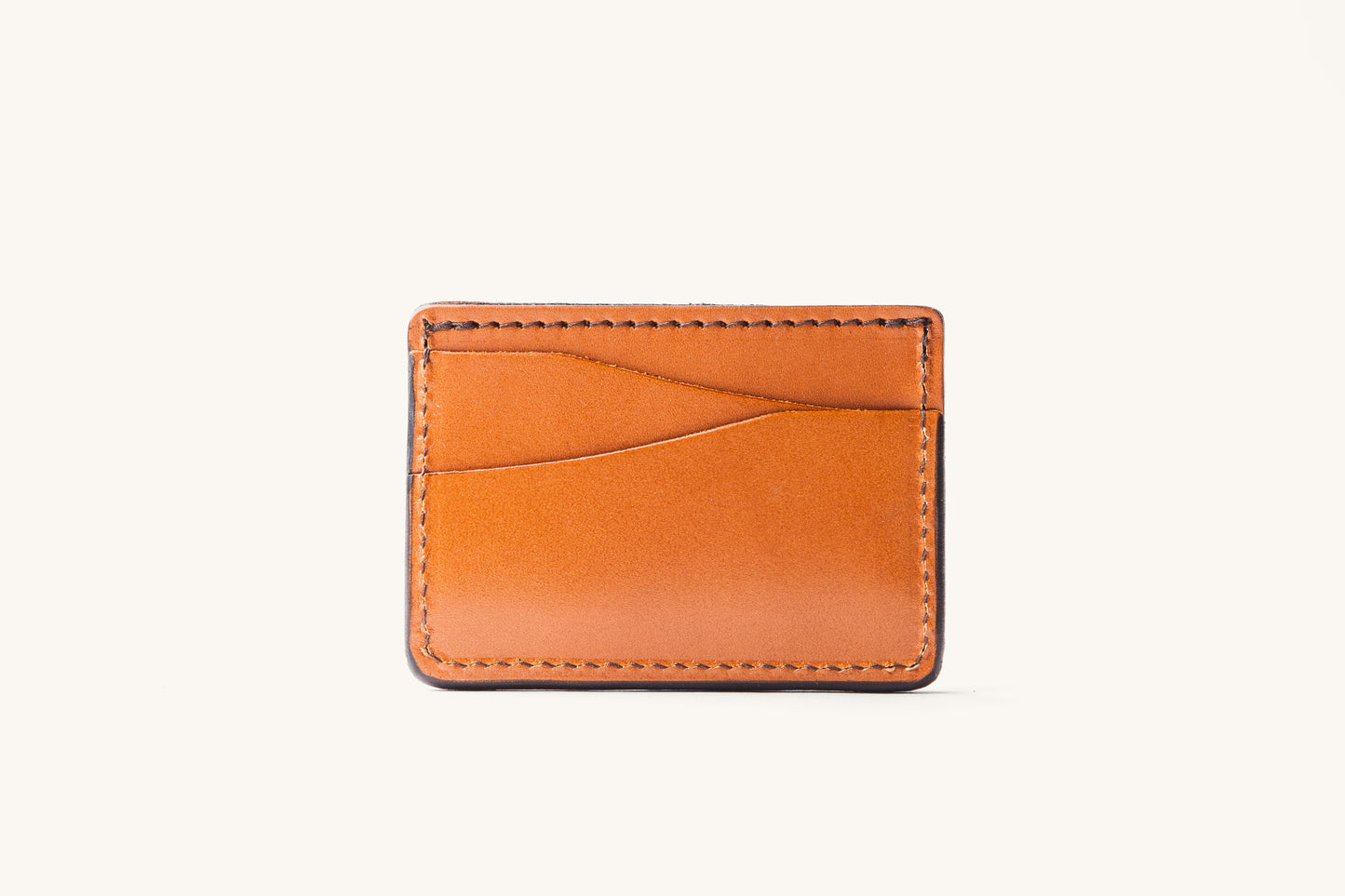 Saddle tan leather wallet with wavy front card slots and dark stitched edges, shown in a front view.