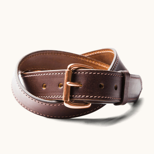 Cognac leather belt with a rose gold-toned buckle and contrast stitching, artfully coiled.