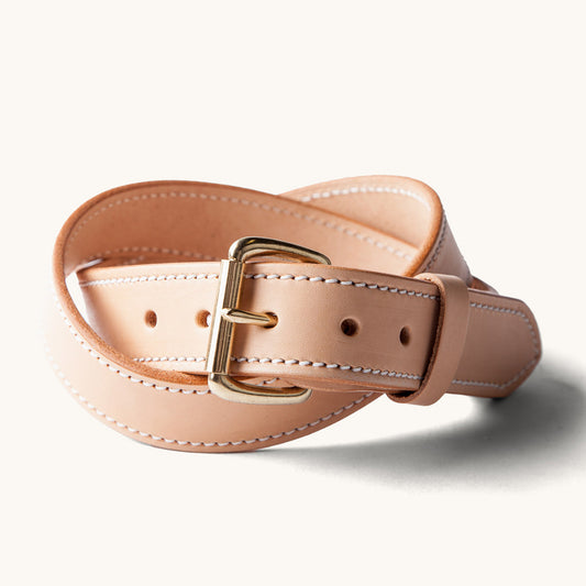Heritage natural leather belt, coiled with visible white stitching and a golden brass buckle.