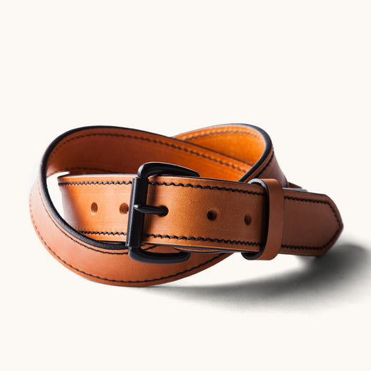 Saddle tan leather belt with black stitching and a black metal buckle, coiled on a white background.