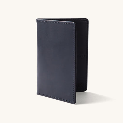 Black leather travel wallet standing upright, slightly open, featuring a smooth finish and visible stitching.