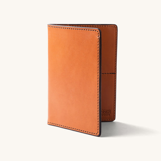 Saddle tan leather travel wallet, standing upright and slightly open, showing visible stitching and partially embossed text.