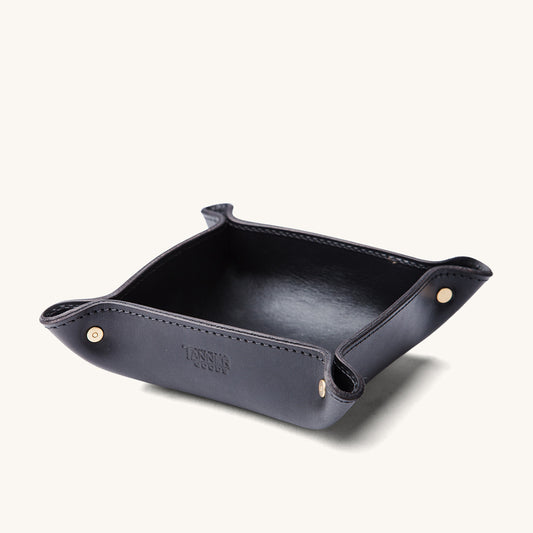 Black leather valet tray with brass snap corners, stitched edges, and an embossed logo.