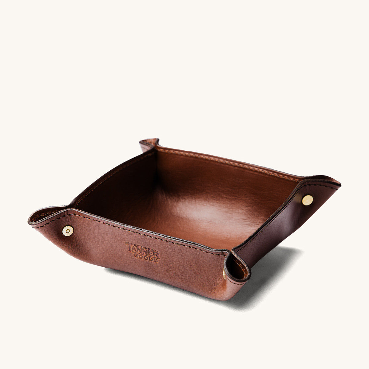 Cognac leather valet tray with brass snap corners and debossed logo.