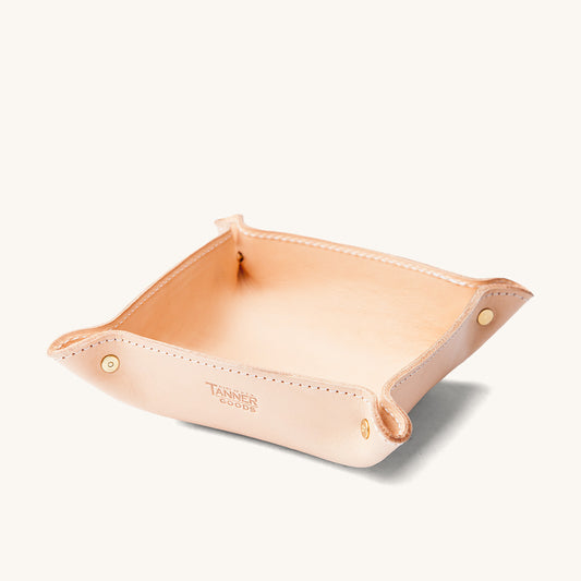 Natural leather valet tray by Tanner Goods with brass fasteners and stitched edges, angled on a white background.