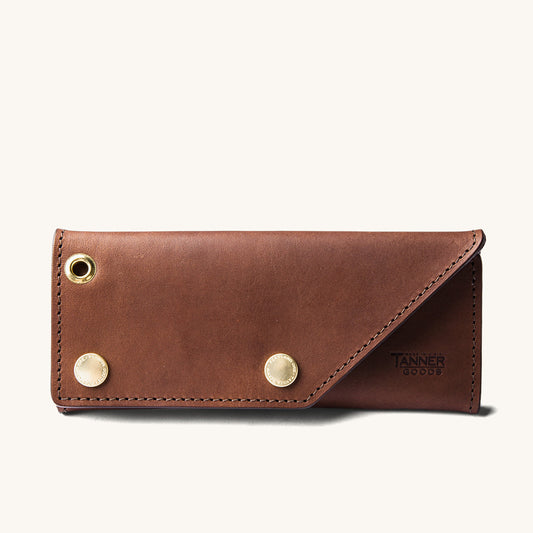 Cognac leather Workman Wallet by Tanner Goods with two brass snap buttons, a grommet, and diagonal flap closure.