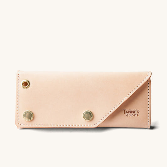 Natural leather Workman Wallet by Tanner Goods with a diagonal flap closure, a gold-toned eyelet, and two embossed snaps.