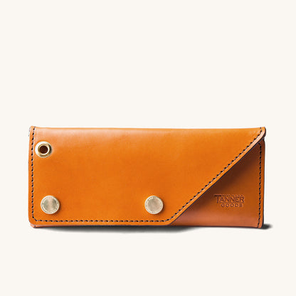 Saddle tan leather Workman Wallet by Tanner Goods with a brass eyelet, two snaps, and diagonal black stitching.